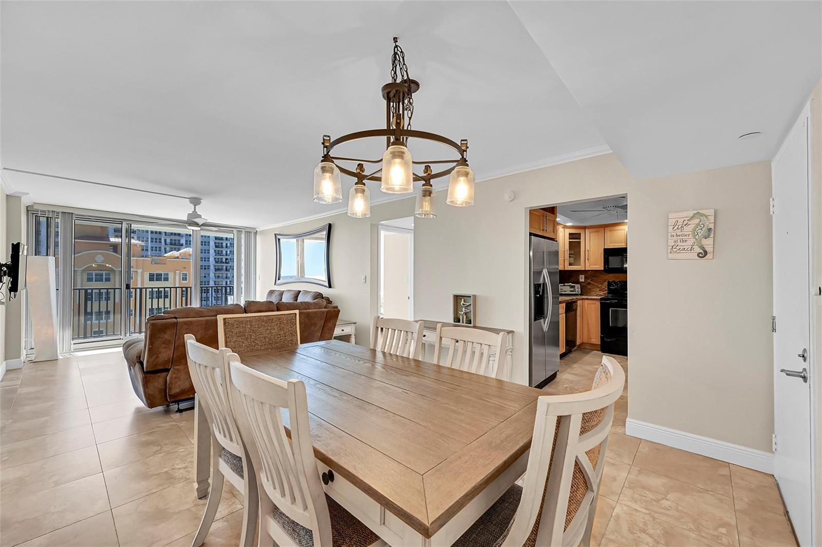 A dining area with a wooden table and chairs sits adjacent to a kitchen and living room — 525 N Ocean Boulevard # 919, Pompano Beach FL 33062, POMPANO BEACH, FL