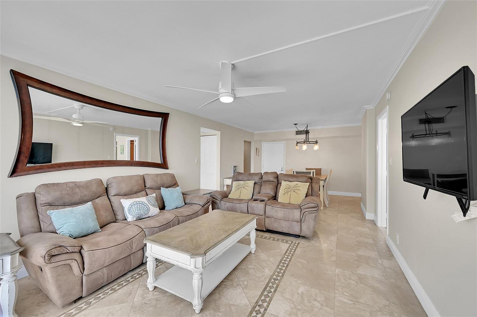 A living room features light tile floors, two brown reclining sofas, and a wall-mounted television — 525 N Ocean Boulevard # 919, Pompano Beach FL 33062, POMPANO BEACH, FL