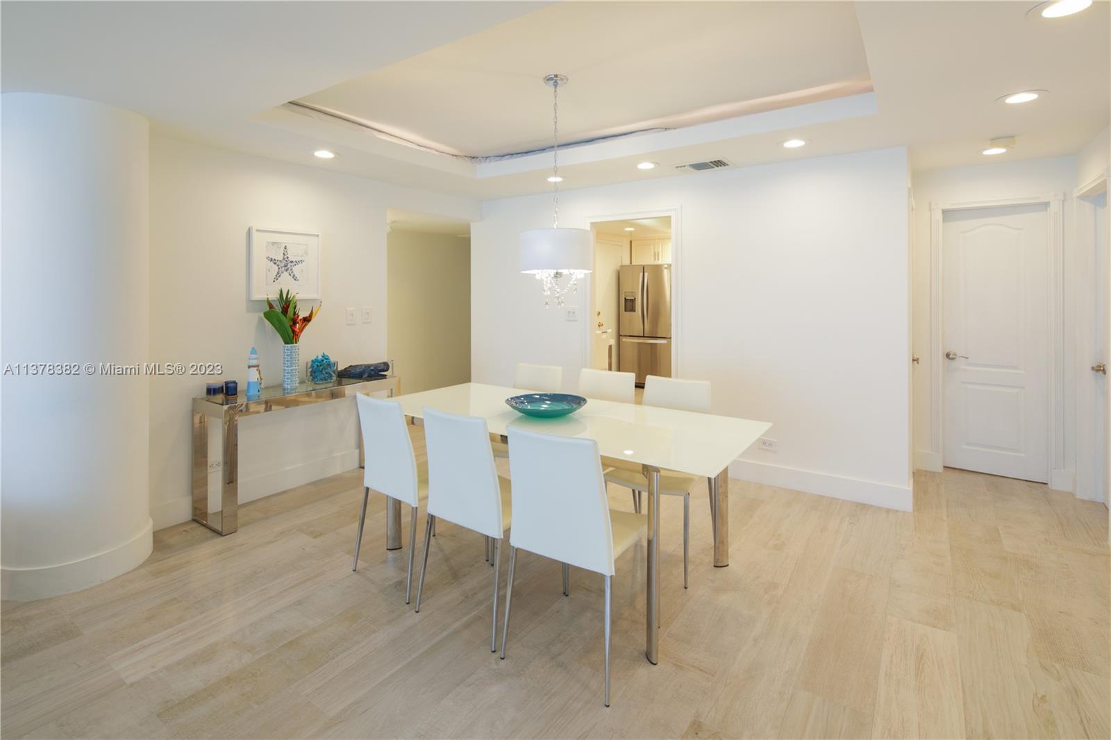 A dining room features a white table, six chairs, a chandelier, and light wood flooring — 5005 Collins Ave # 610, Miami Beach FL 33140, MIAMI BEACH, FL