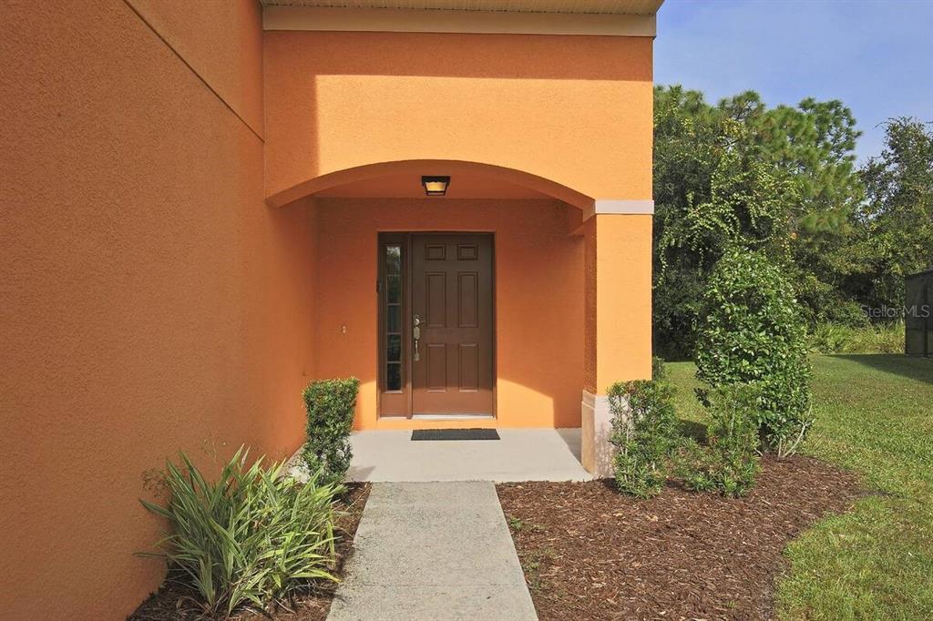 A concrete walkway leads to the covered front entrance of an orange stucco house — 2660 SANTOSH COVE, KISSIMMEE, FL