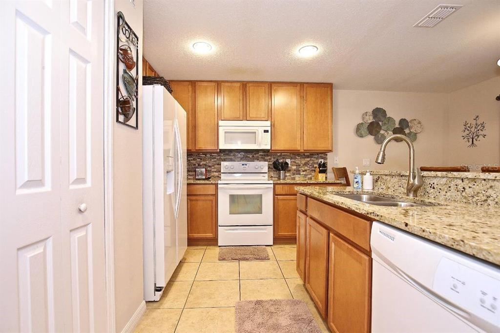 A kitchen with wood cabinets, granite countertops, tile flooring, and white appliances — 2660 SANTOSH COVE, KISSIMMEE, FL
