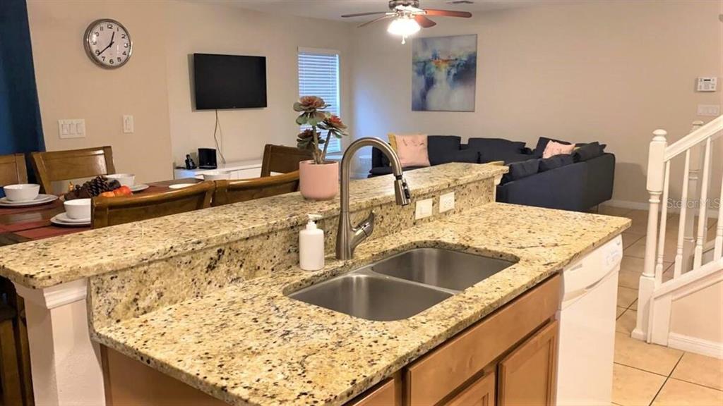 A kitchen island with a granite countertop and stainless steel sink overlooks a living area — 2660 SANTOSH COVE, KISSIMMEE, FL