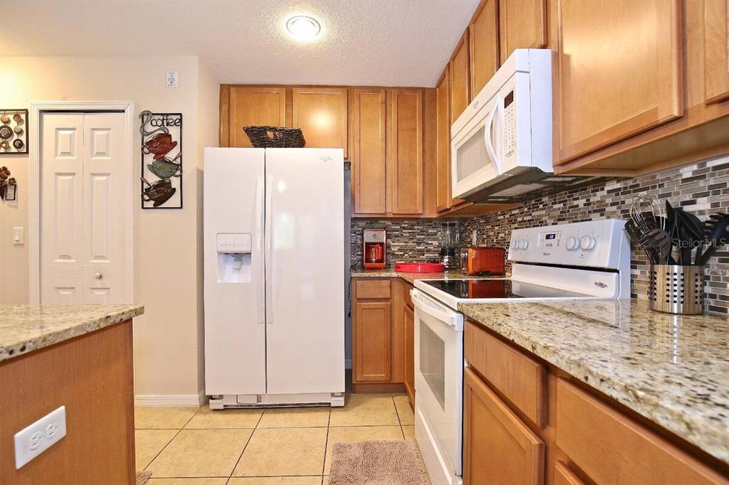 A kitchen features wood cabinets, granite countertops, a white refrigerator, and a tiled backsplash — 2660 SANTOSH COVE, KISSIMMEE, FL