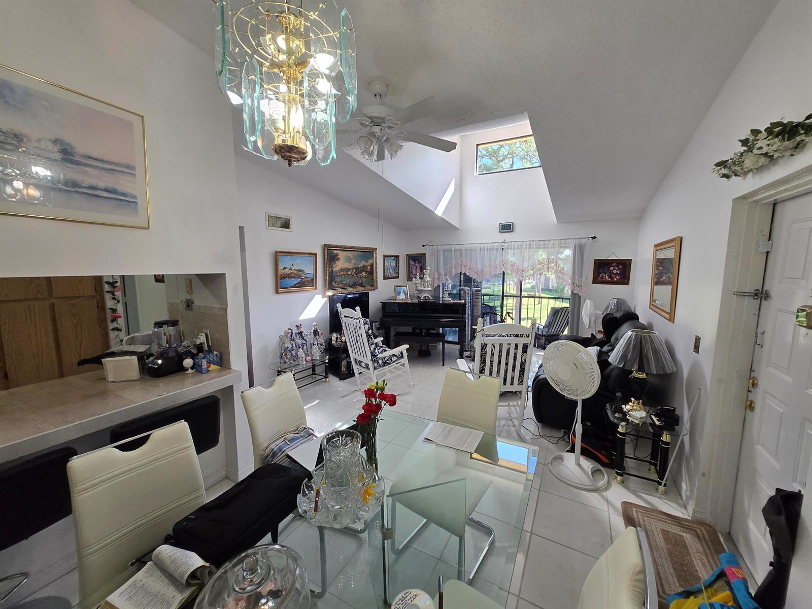 A dining area with a glass table and white chairs opens into a vaulted living room — 819 Sky Pine Way # G3, FL 33415, FL
