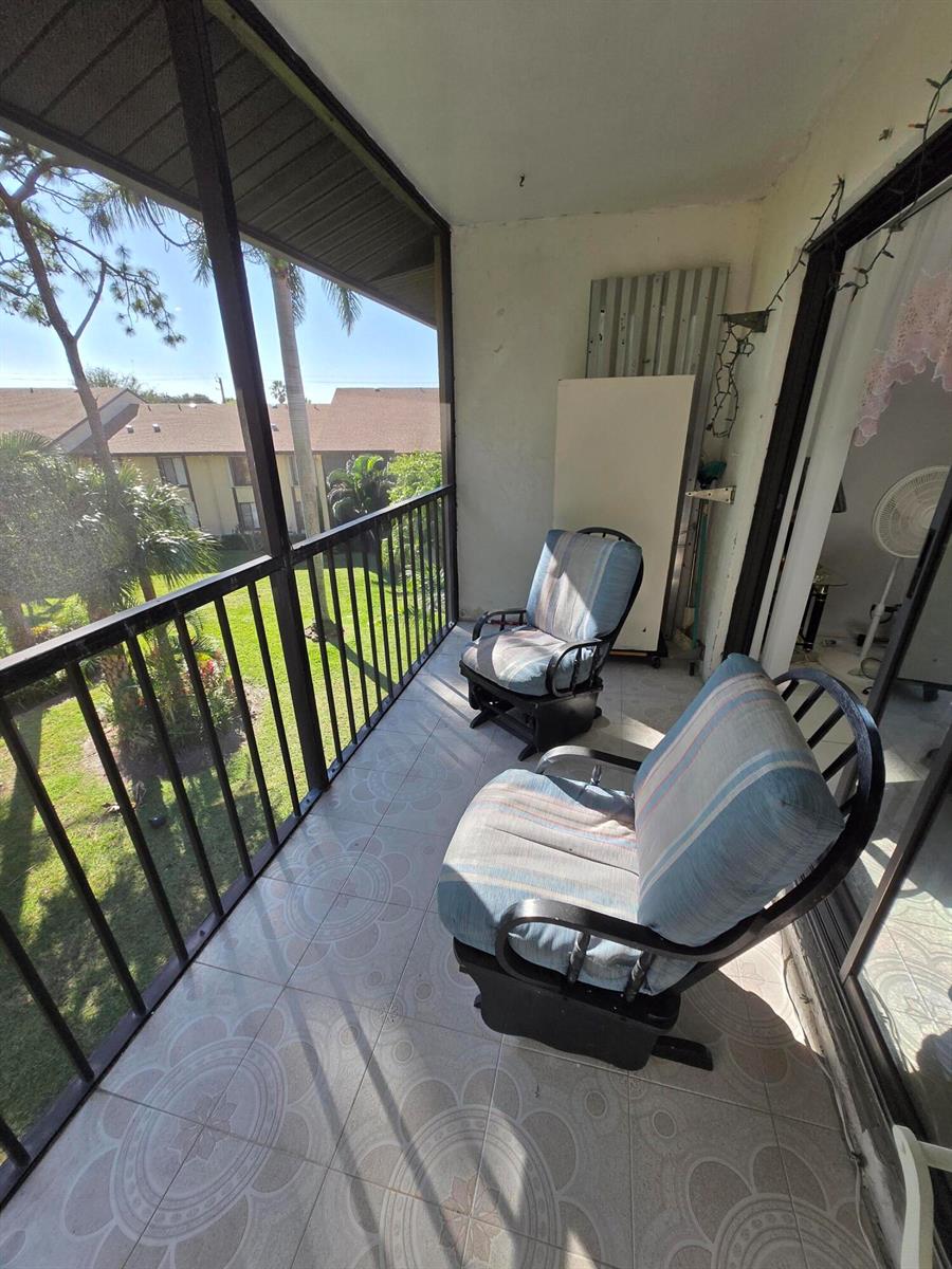 A screened-in balcony features tiled flooring, two rocking chairs, and a view of the grounds — 819 Sky Pine Way # G3, FL 33415, FL