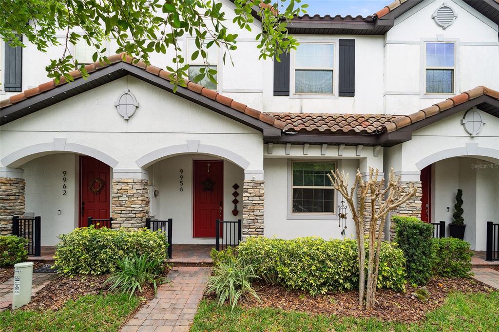 The exterior of a two-story townhouse features white stucco walls, red doors, and tiled roofs — 9956 EAGLE CREEK CENTER BLVD, ORLANDO, FL