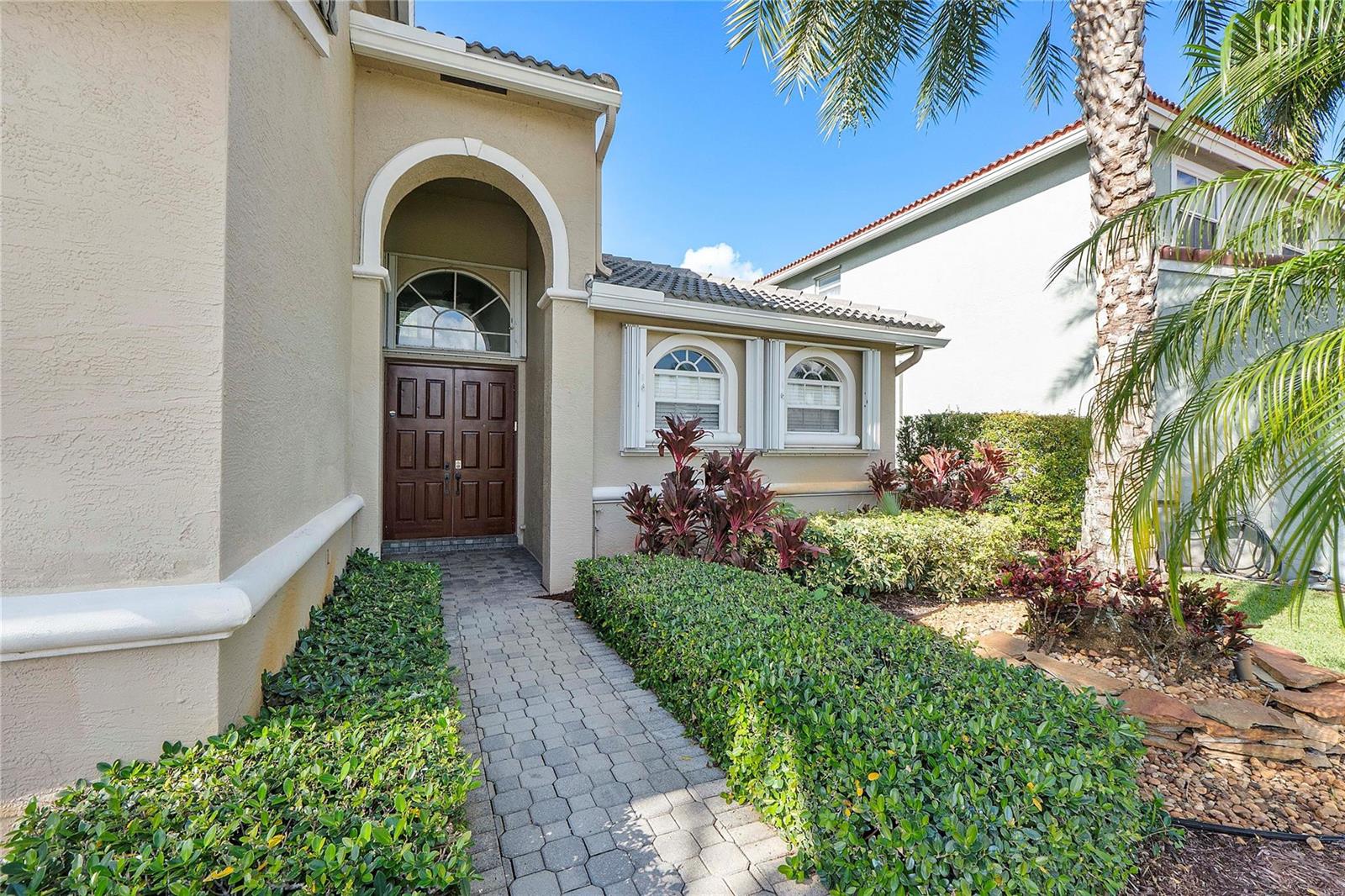 A paved walkway leads to the arched entryway of a tan house with a double door — 11353 Sea Grass Circle, Boca Raton FL 33498, BOCA RATON, FL