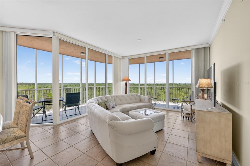 A living room with a white sectional sofa, tile floors, and floor-to-ceiling windows overlooking trees — 3191 MATECUMBE KEY ROAD UNIT 202, PUNTA GORDA, FL