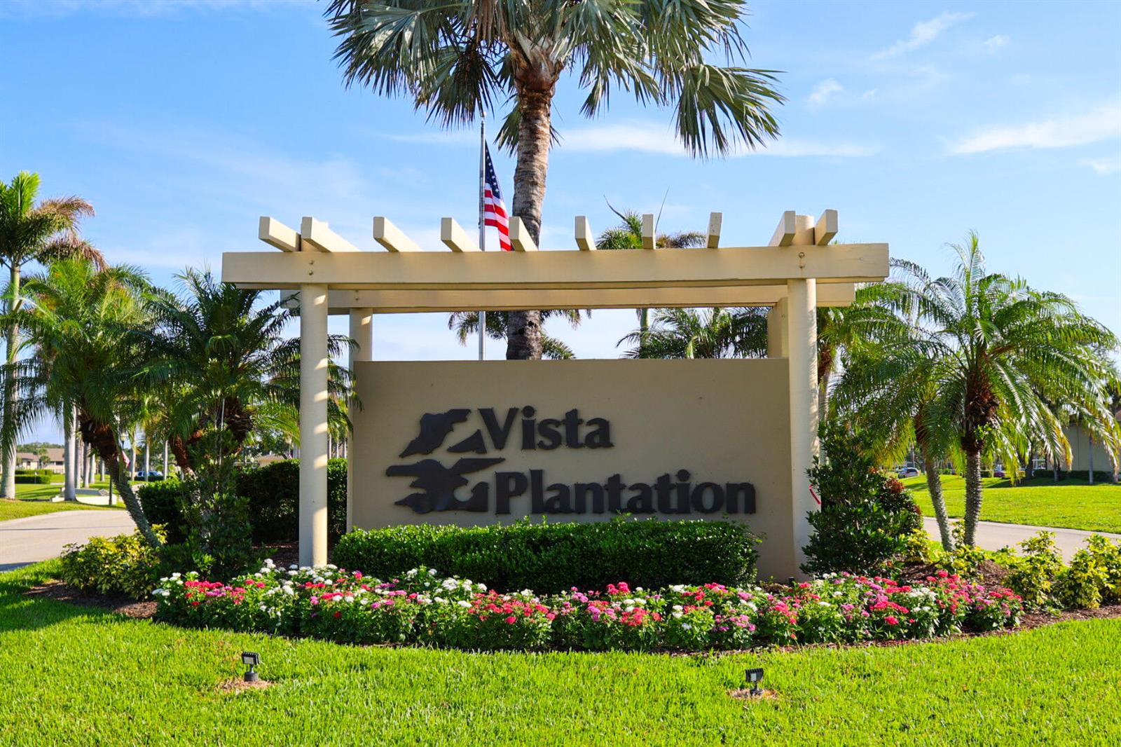 A sign for Vista Plantation stands in a landscaped area with palm trees and flowers — 29 Plantation Drive # 202, Vero Beach FL 32966, VERO BEACH, FL