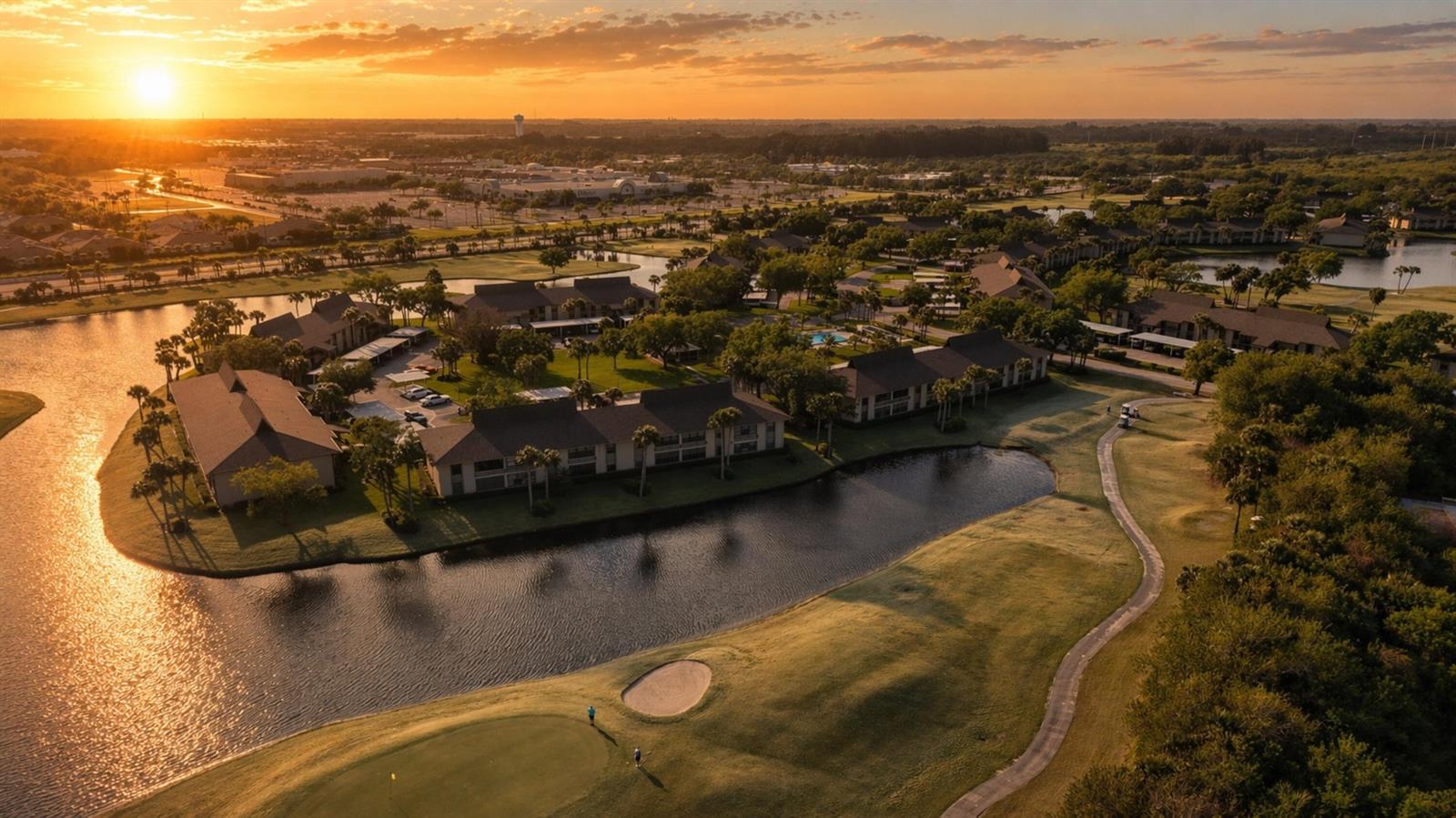 An aerial view of a golf course community with multi-family buildings surrounding a lake at sunset — 29 Plantation Drive # 202, Vero Beach FL 32966, VERO BEACH, FL