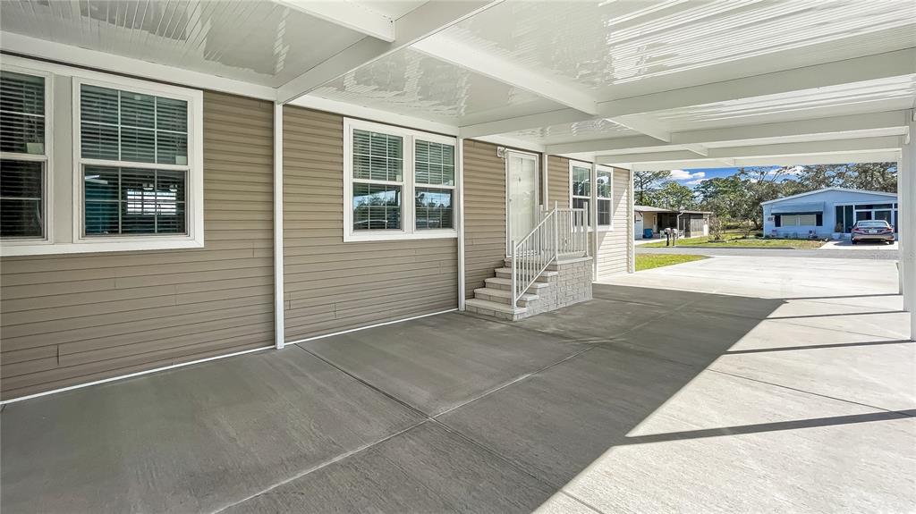 A covered concrete carport leads to the entrance of a house with tan vinyl siding — 9896 SCEPTER AVENUE, BROOKSVILLE, FL