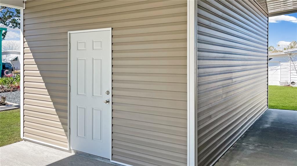A white door is set into the beige vinyl-sided exterior wall of a storage shed — 9896 SCEPTER AVENUE, BROOKSVILLE, FL