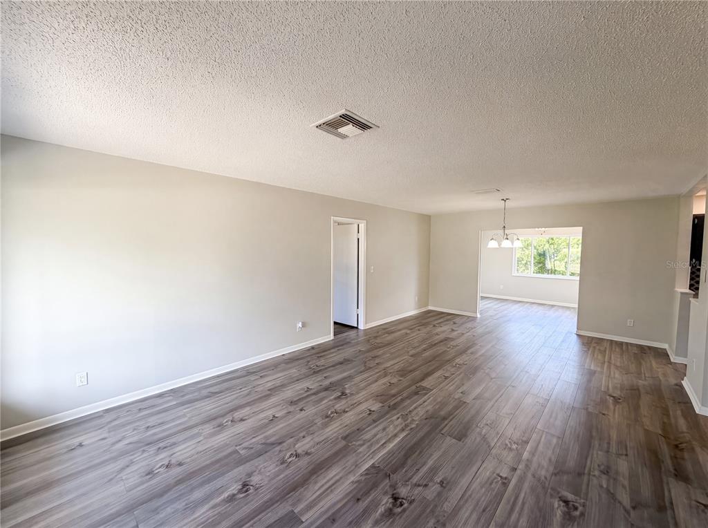 An open living area features light gray walls, wood-look flooring, and a ceiling air vent — 9281 BAY DRIVE, SPRING HILL, FL