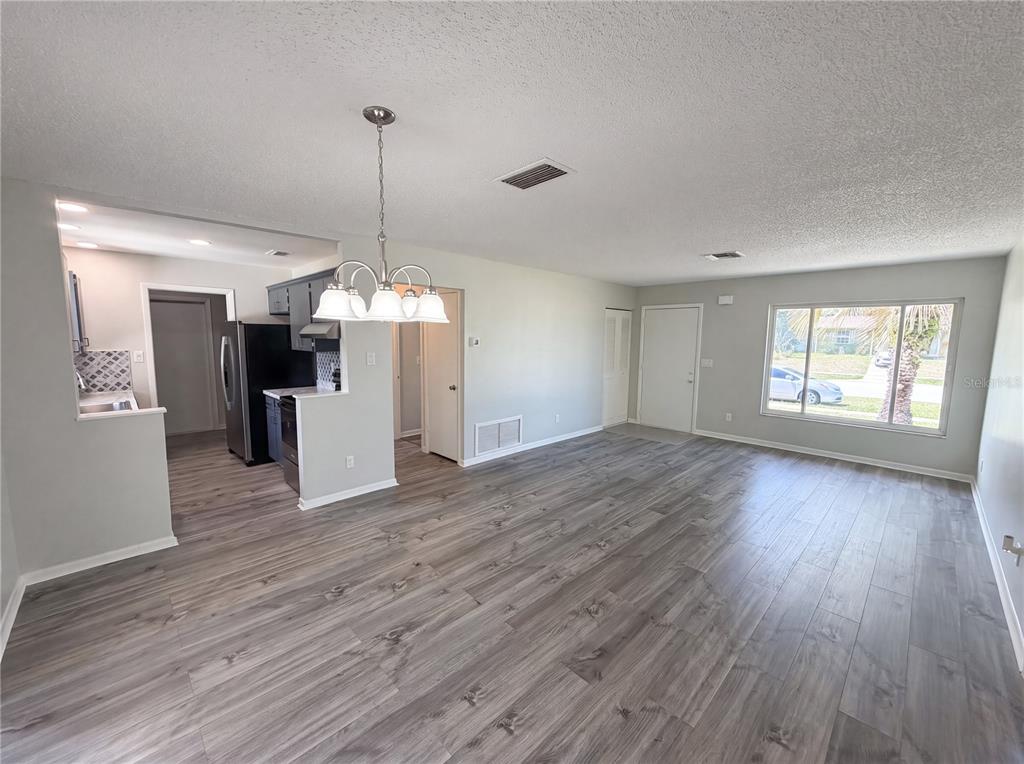 An open-concept living and dining area features gray wood-look flooring and a kitchen pass-through — 9281 BAY DRIVE, SPRING HILL, FL