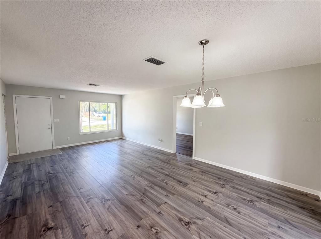 An open living and dining area features gray wood-look flooring and a hanging light fixture — 9281 BAY DRIVE, SPRING HILL, FL