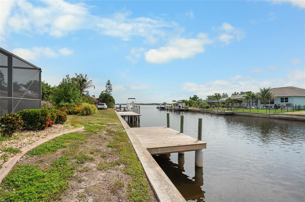 A wooden dock extends into a canal behind a residential property with a screened patio — 3098 MAUCK TERRACE, PORT CHARLOTTE, FL