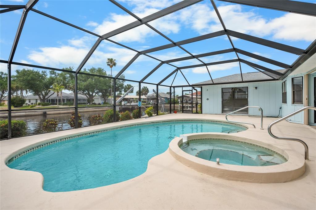 A screened-in pool and hot tub area overlooking a canal with a blue sky — 3098 MAUCK TERRACE, PORT CHARLOTTE, FL