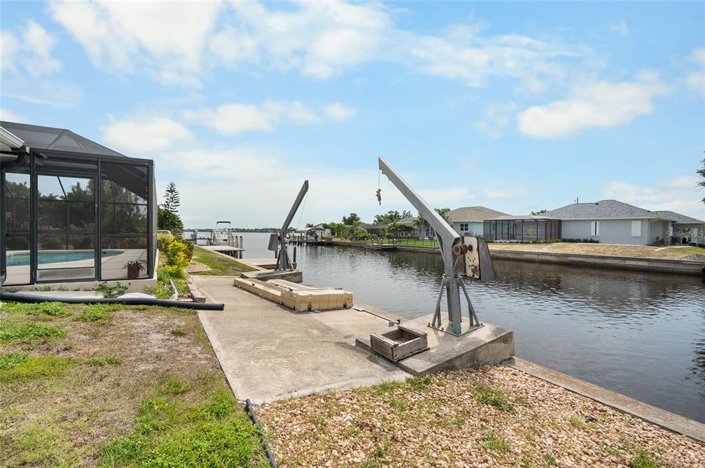 A concrete dock area features two boat lifts along a canal behind a residential home — 3098 MAUCK TERRACE, PORT CHARLOTTE, FL