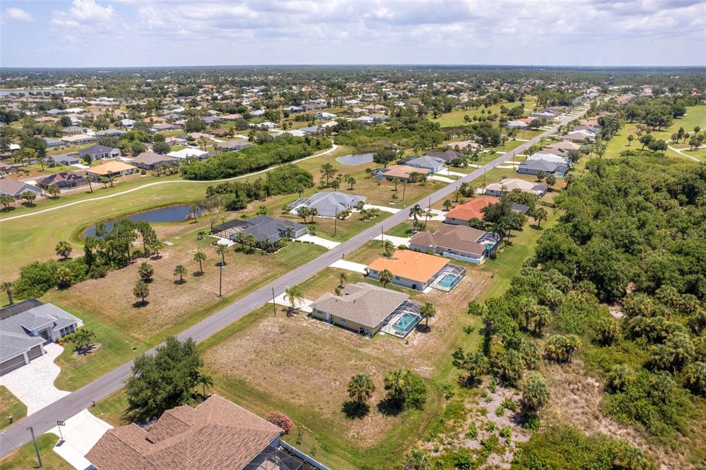 An aerial view shows a residential street lined with houses, pools, and surrounding green space — 74 LONG MEADOW COURT, ROTONDA WEST, FL