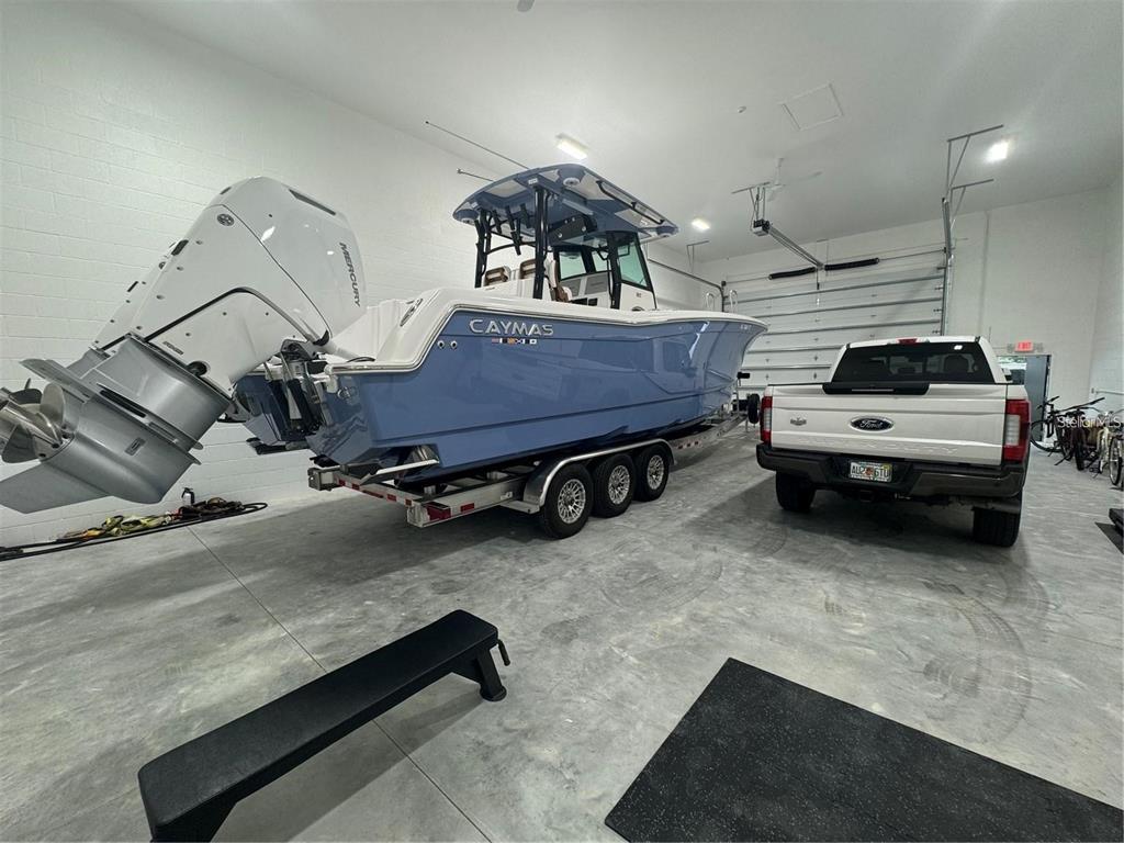 A light blue Caymas boat on a trailer is parked inside a spacious white garage — 25155 AIRPORT ROAD UNIT D2, PUNTA GORDA, FL