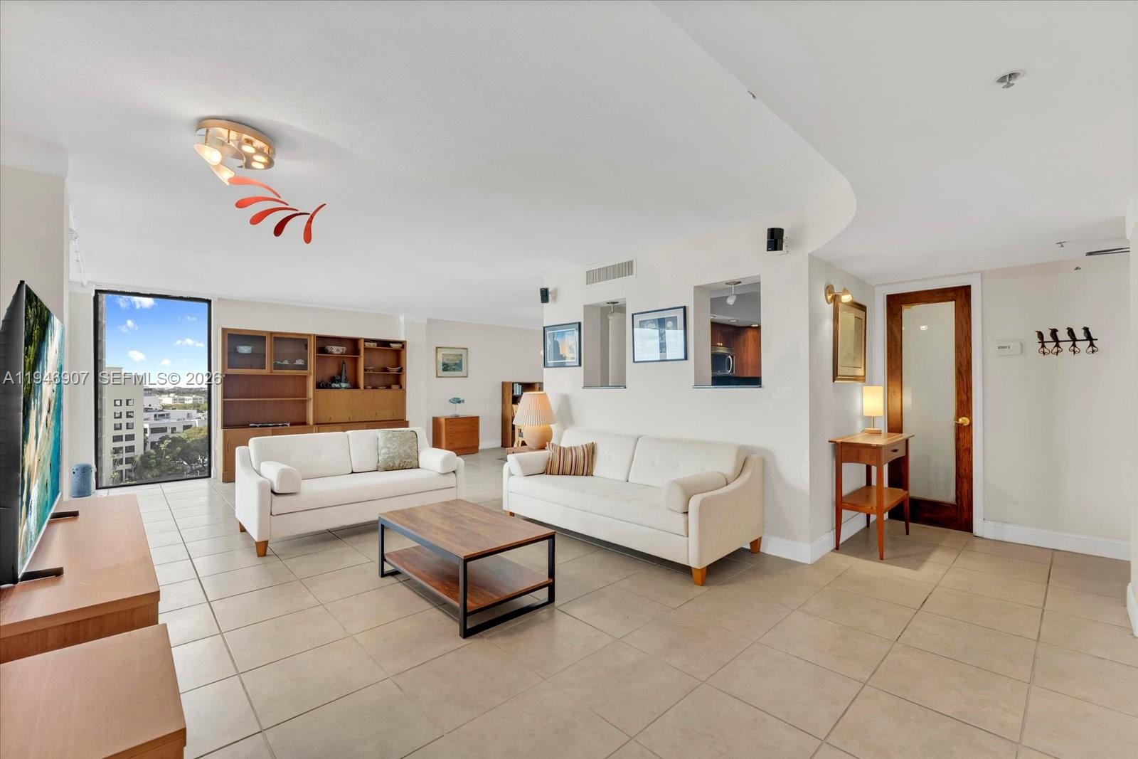 A living room features white sofas, a wooden coffee table, tile floors, and large windows — 2843 S Bayshore Dr # 11C, Miami FL 33133, MIAMI, FL