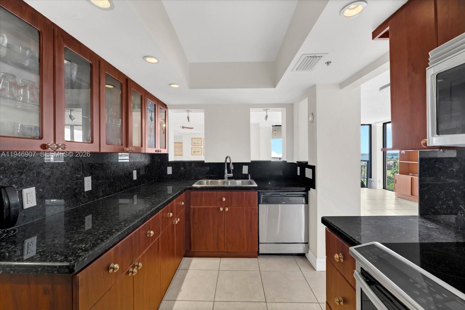 A kitchen features dark wood cabinets, black granite countertops, stainless steel appliances, and tile flooring — 2843 S Bayshore Dr # 11C, Miami FL 33133, MIAMI, FL