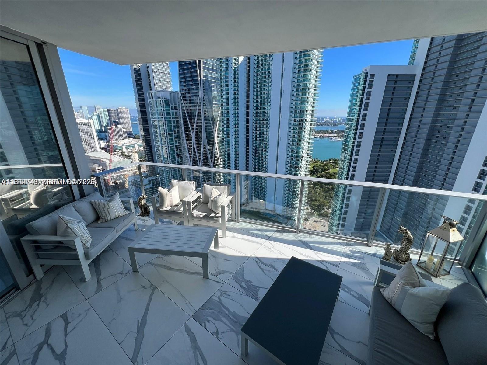 A high-rise balcony features marble-look tile flooring, outdoor furniture, and panoramic city and water views — 851 NE 1st Ave # 3903, Miami FL 33132, MIAMI, FL