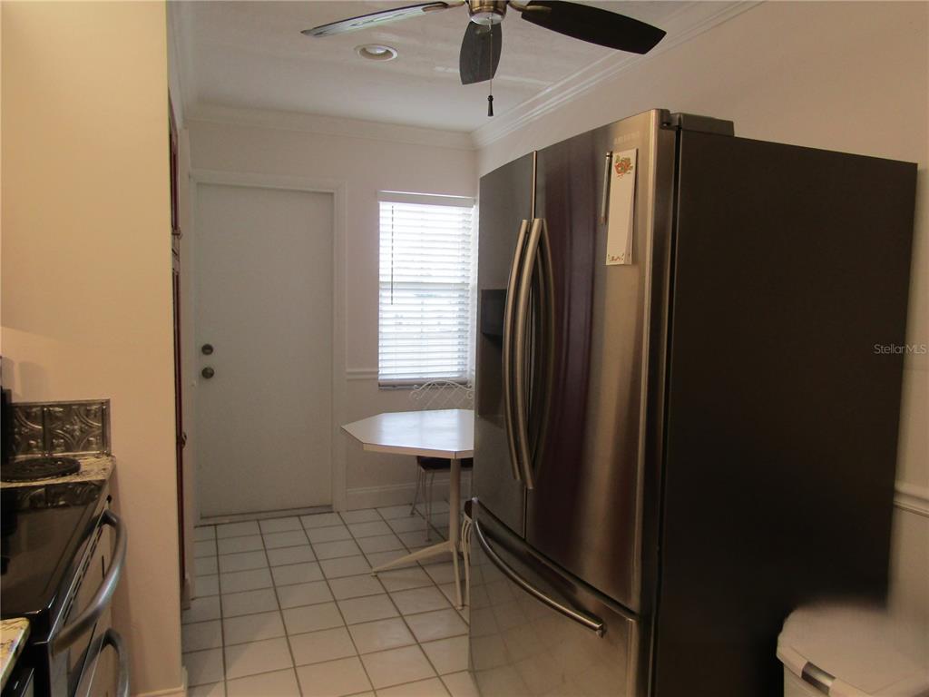 A kitchen features white tile flooring, a stainless steel refrigerator, and a small dining table — 7351 W COUNTRY CLUB DRIVE N UNIT 202, SARASOTA, FL