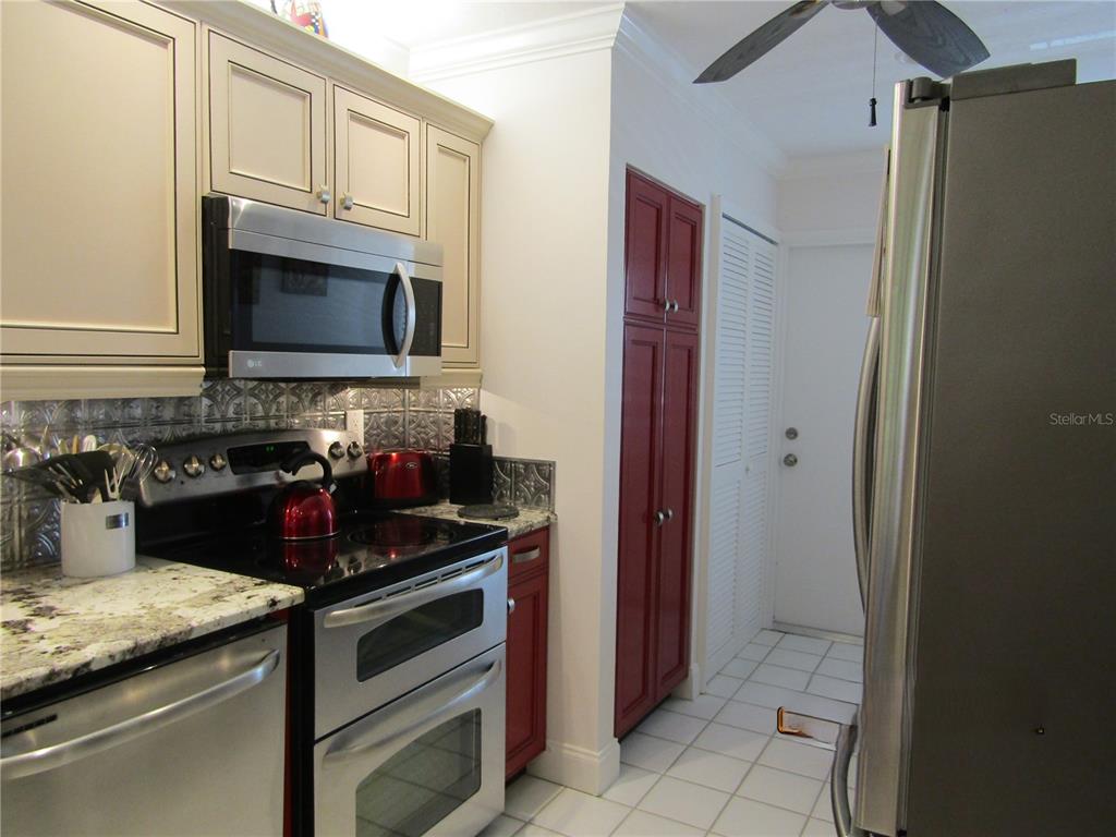 A kitchen features stainless steel appliances, cream cabinets, a red pantry, and a tiled backsplash — 7351 W COUNTRY CLUB DRIVE N UNIT 202, SARASOTA, FL