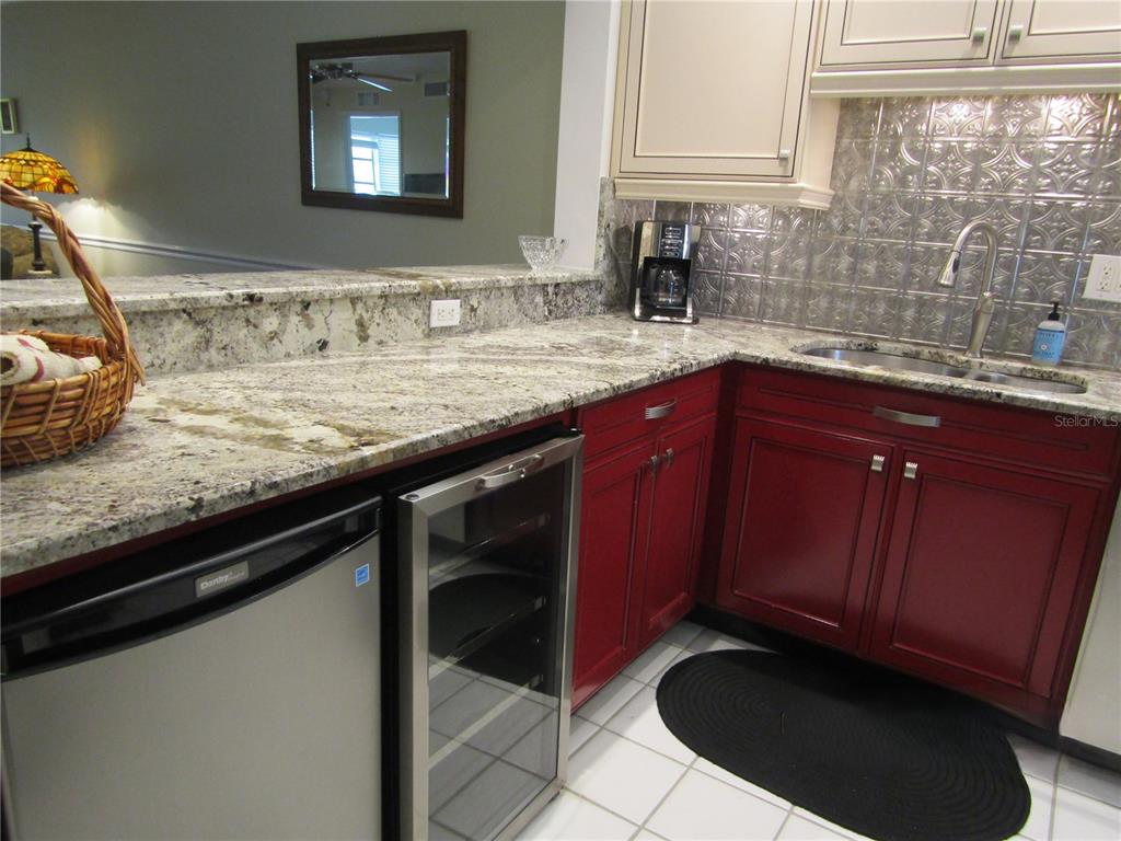 A kitchen features red cabinets, granite countertops, a stainless steel wine cooler, and a metal backsplash — 7351 W COUNTRY CLUB DRIVE N UNIT 202, SARASOTA, FL