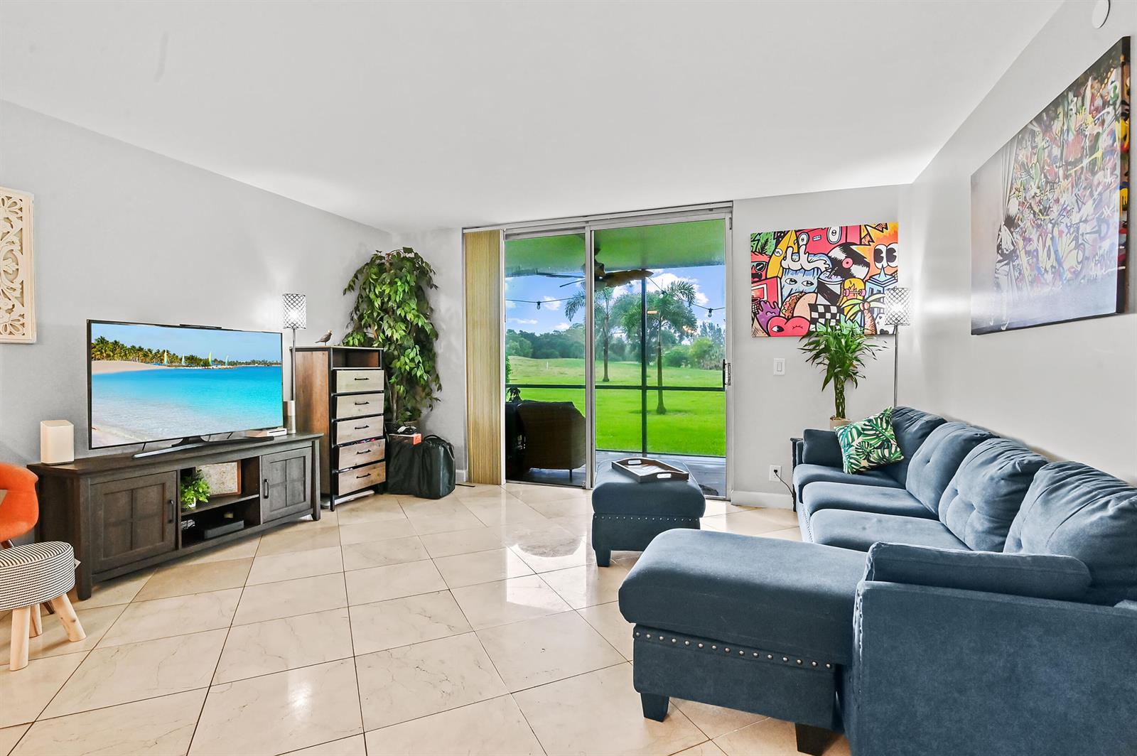 A living room features a blue sectional sofa, a television on a console, and sliding doors — 6400 NW 2nd Avenue # 124, Boca Raton FL 33487, BOCA RATON, FL