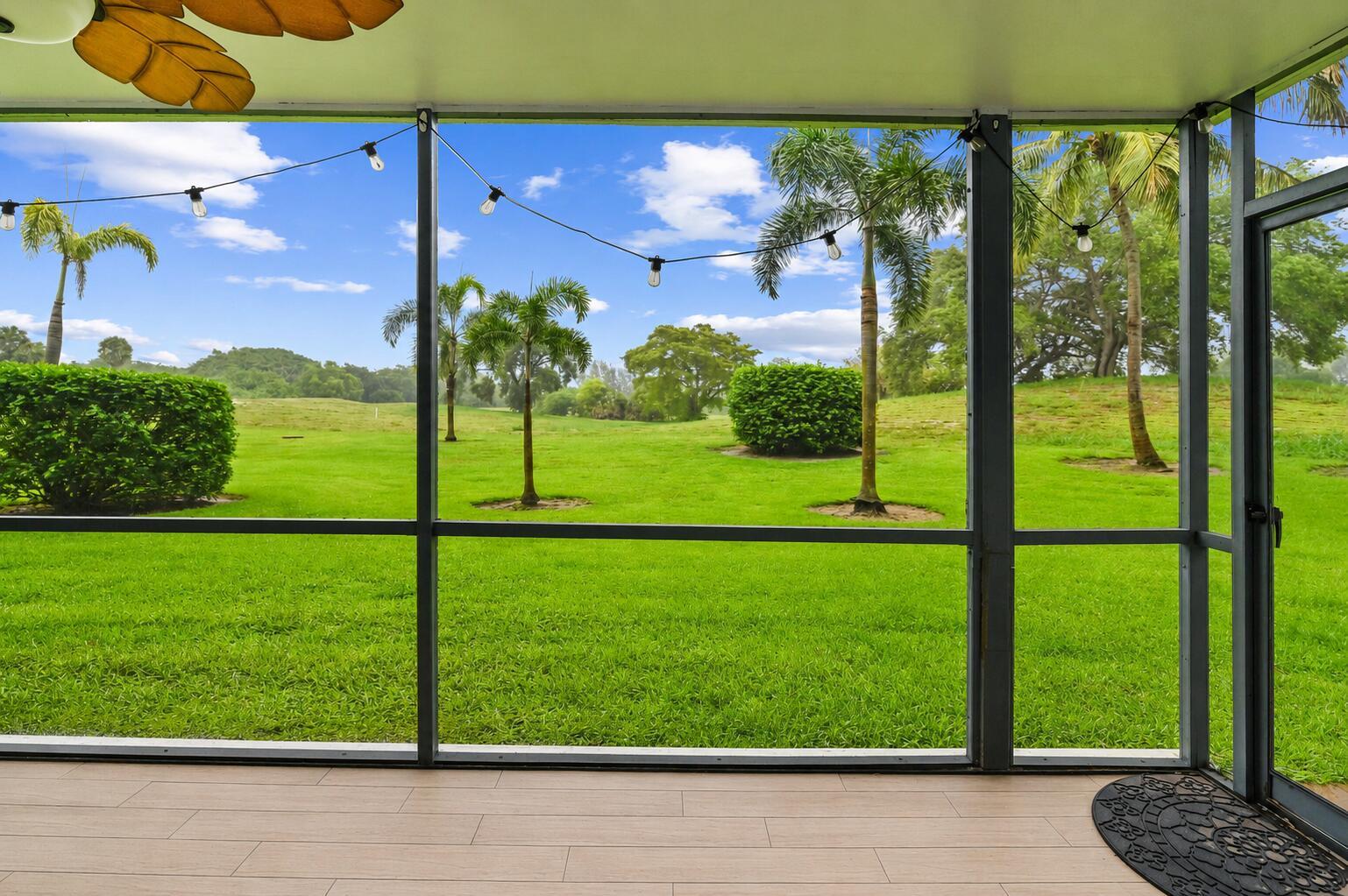 A screened-in patio with light wood-look tile flooring overlooks a grassy yard with palm trees — 6400 NW 2nd Avenue # 124, Boca Raton FL 33487, BOCA RATON, FL