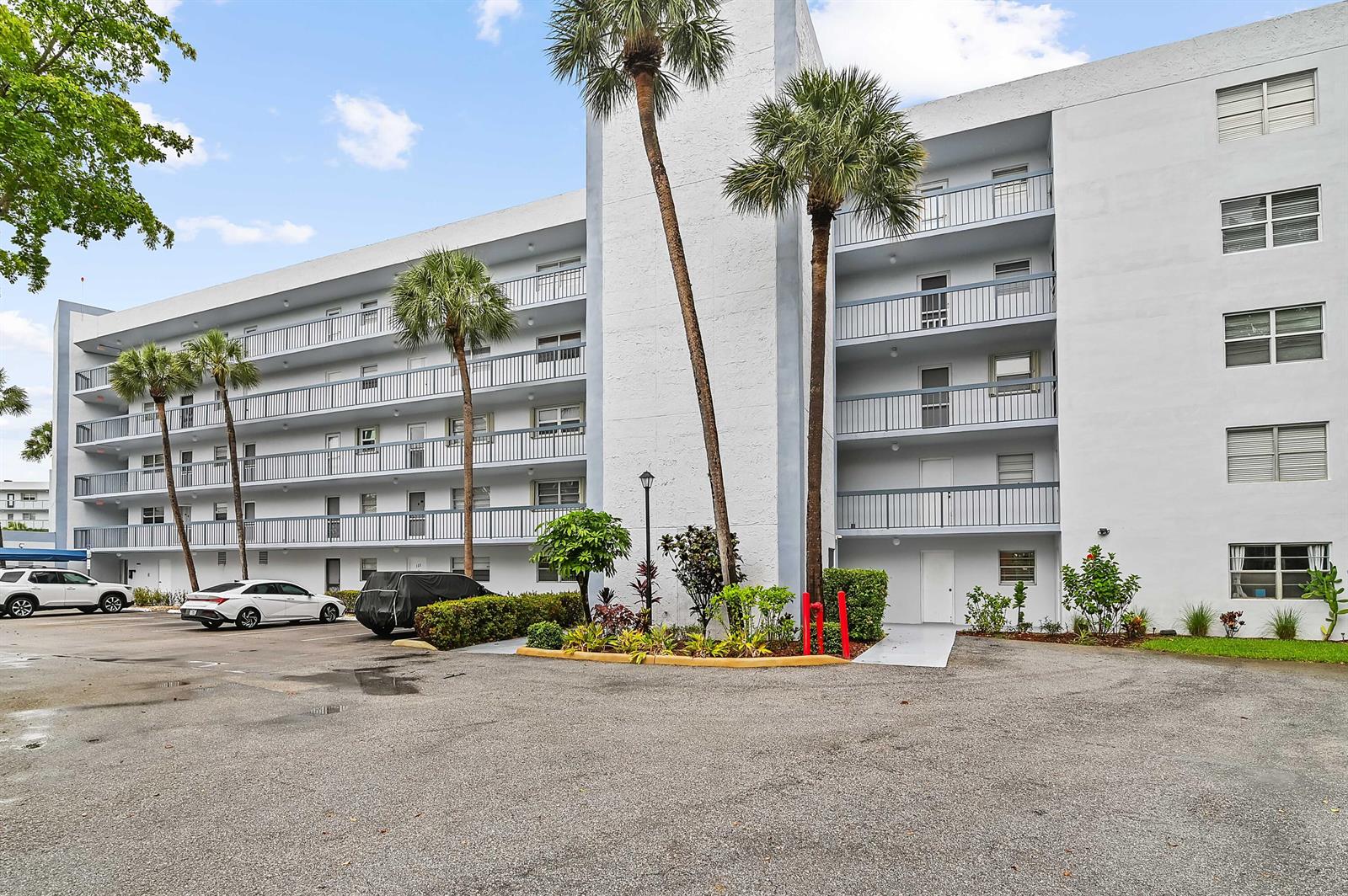 A multi-story white apartment building with balconies and palm trees in a parking lot — 6400 NW 2nd Avenue # 124, Boca Raton FL 33487, BOCA RATON, FL