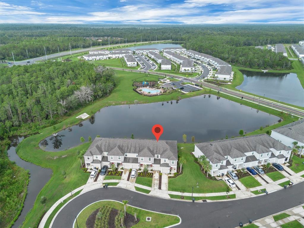 An aerial view shows a townhome community with a lake, swimming pool, and surrounding woods — 2256 PORTRAIT STREET, KISSIMMEE, FL