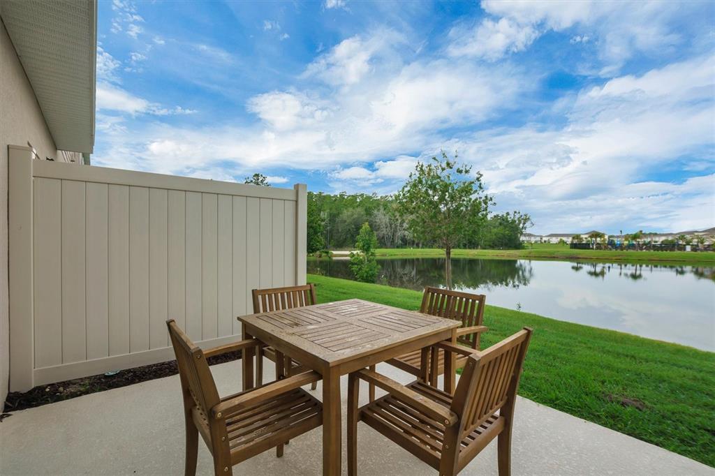 A wooden patio table and chairs sit on a concrete slab overlooking a pond — 2256 PORTRAIT STREET, KISSIMMEE, FL
