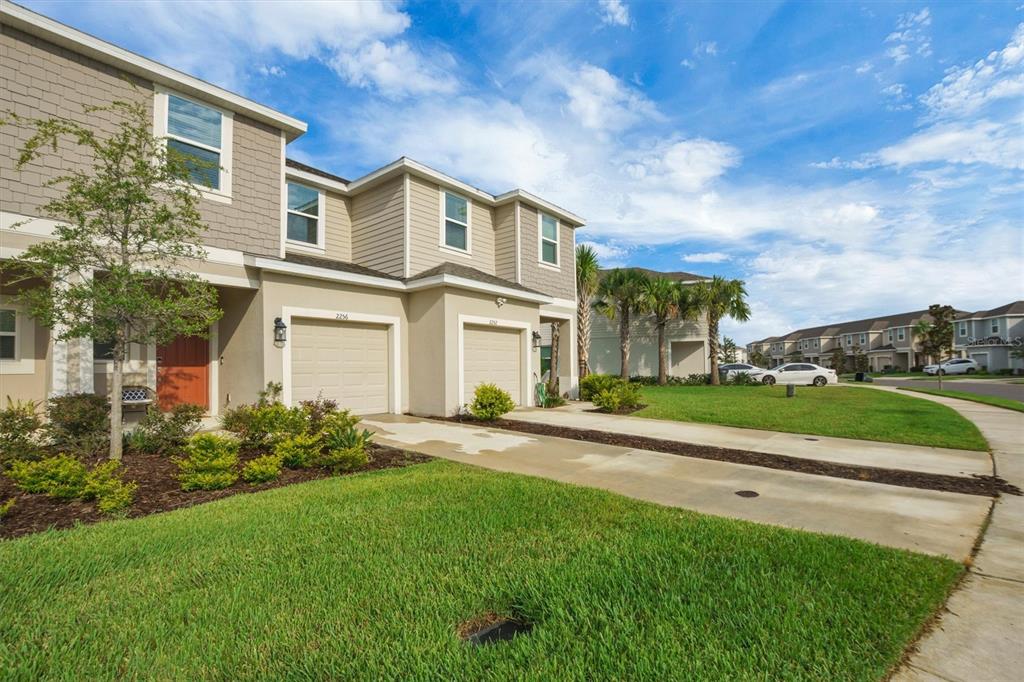 A two-story townhouse exterior with two garage doors, a concrete driveway, and a grassy lawn — 2256 PORTRAIT STREET, KISSIMMEE, FL