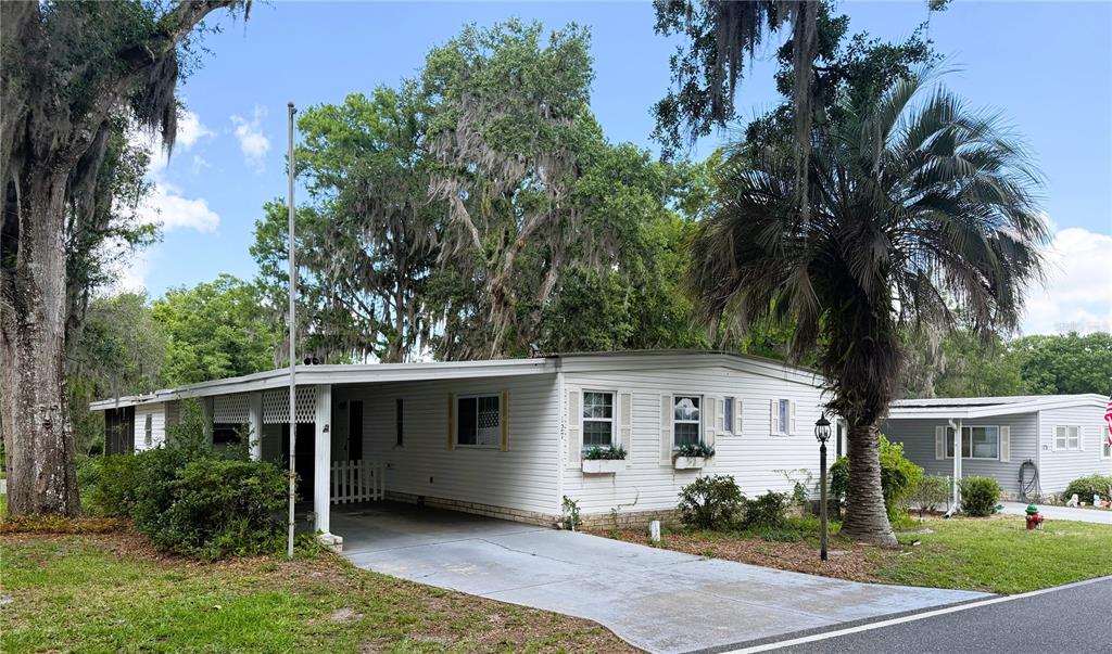 A white mobile home with a carport and a large palm tree in the front yard — 127 ROYAL PALM DRIVE, LEESBURG, FL