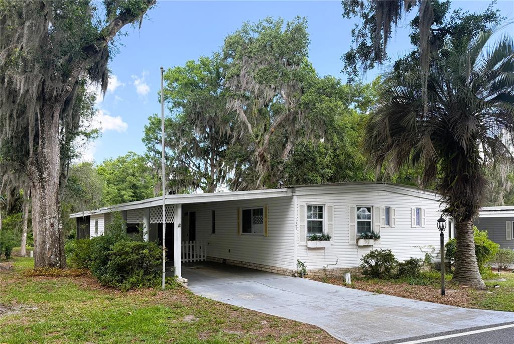 A white mobile home with a carport and a large tree with Spanish moss — 127 ROYAL PALM DRIVE, LEESBURG, FL