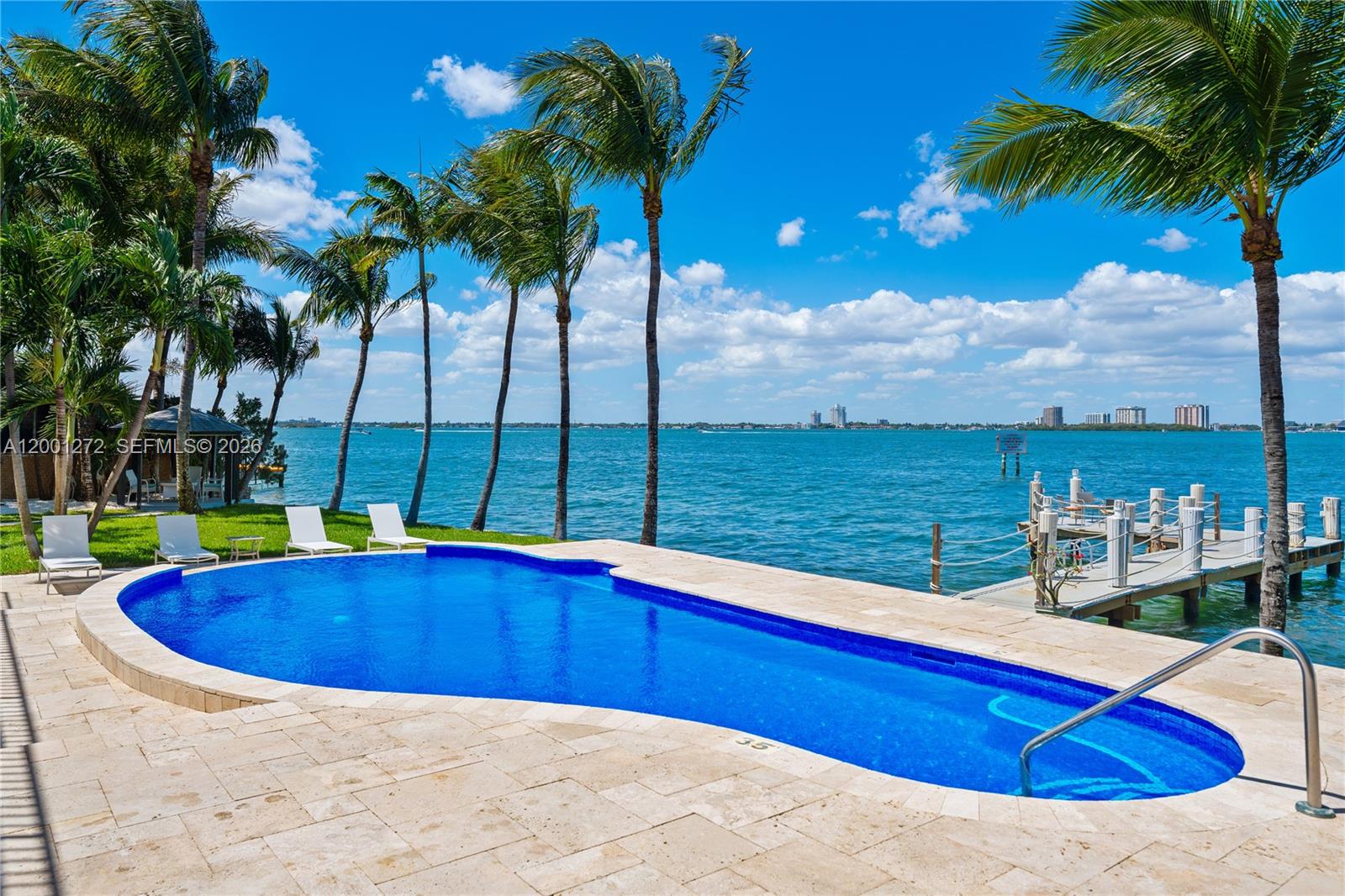 A swimming pool sits on a stone patio overlooking a bay with a wooden dock — 1575 Stillwater Dr, Miami Beach FL 33141, MIAMI BEACH, FL