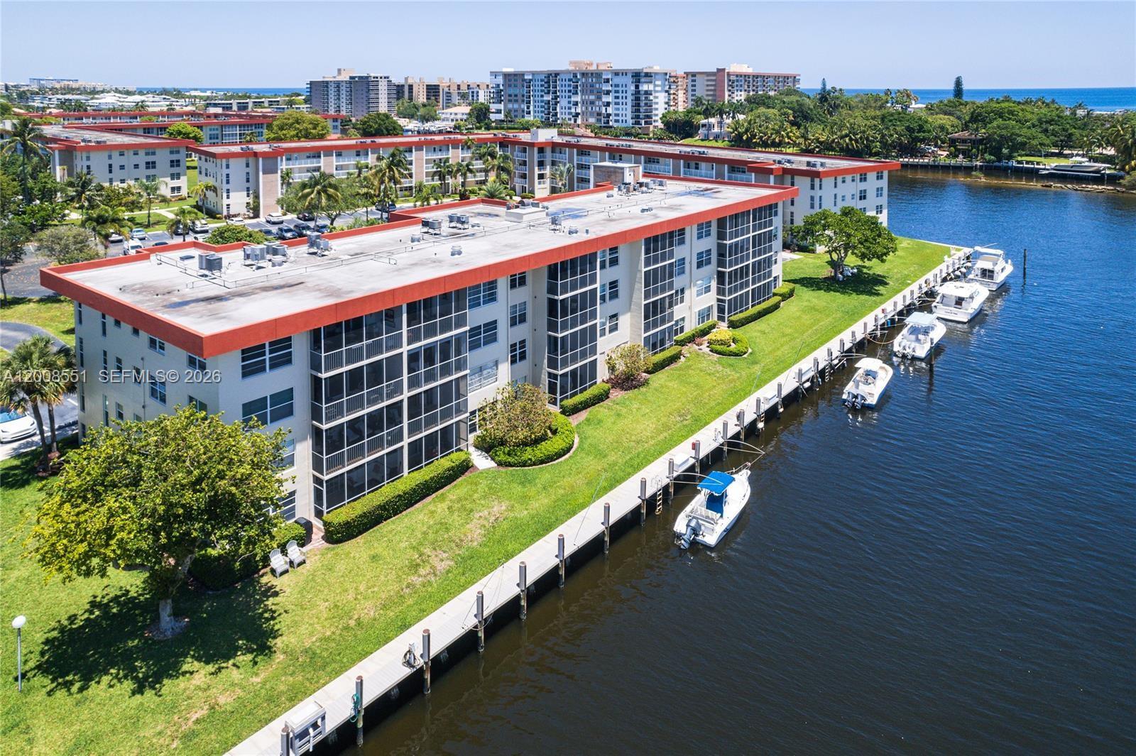 An aerial view shows a multi-story apartment building situated along a canal with docked boats — 3050 NE 48th Ct # 405, Lighthouse Point FL 33064, LIGHTHOUSE POINT, FL