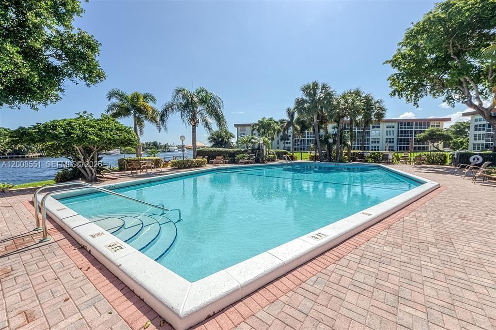 A rectangular swimming pool with steps is surrounded by a brick patio and palm trees — 3050 NE 48th Ct # 405, Lighthouse Point FL 33064, LIGHTHOUSE POINT, FL
