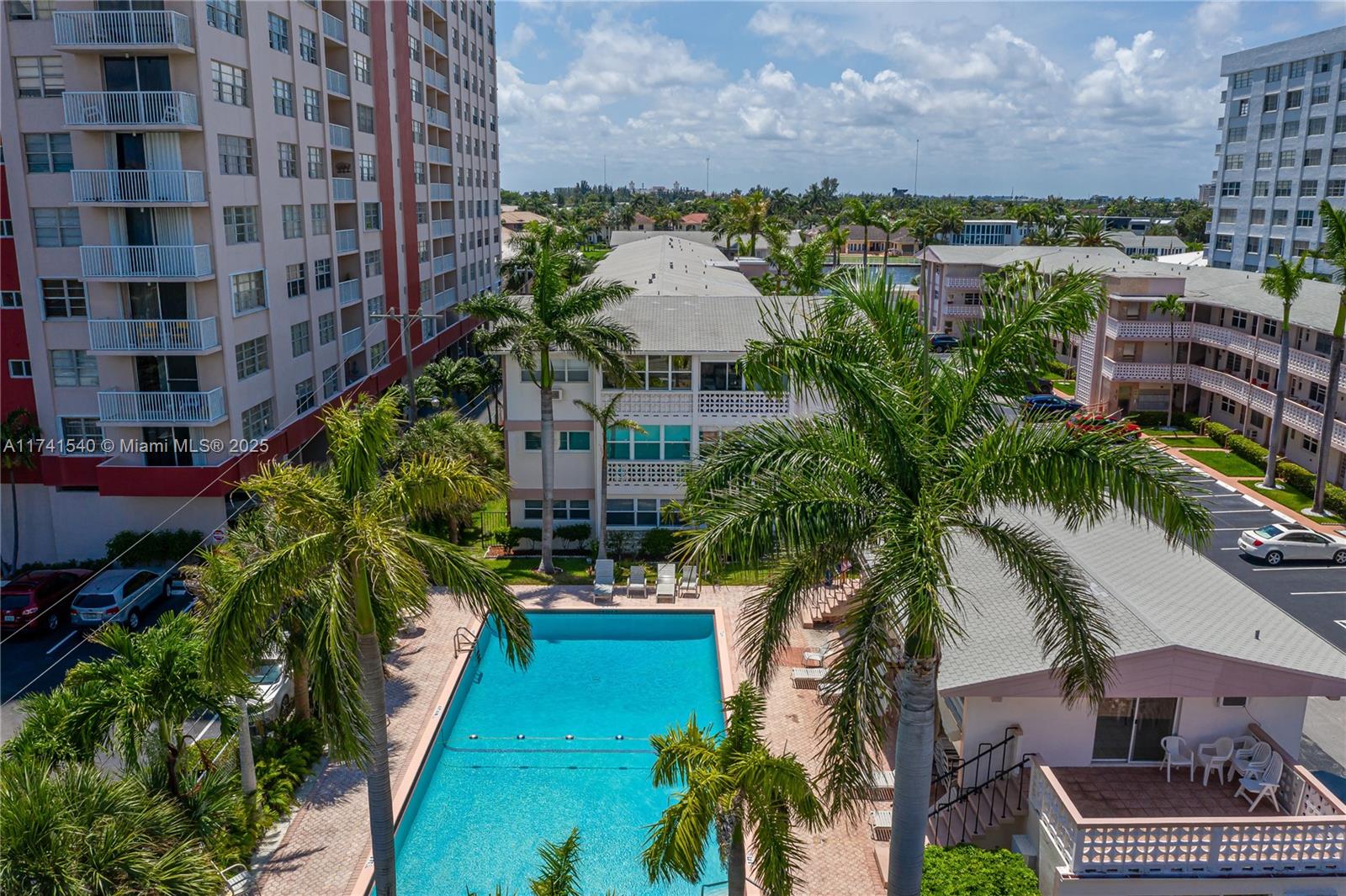 An outdoor swimming pool is surrounded by palm trees and multi-story residential apartment buildings — 3131 S Ocean Dr # 211, Hallandale Beach FL 33009, HALLANDALE BEACH, FL
