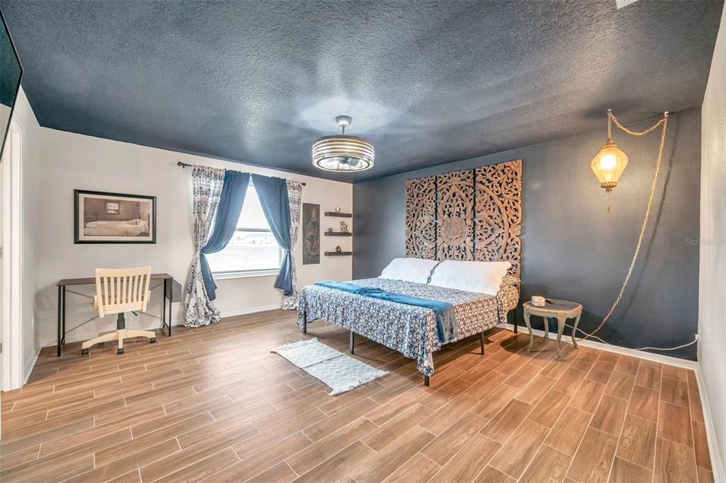 A bedroom features a dark ceiling, wood-look tile floors, and a large carved wooden headboard — 3737 COPPERSPRING BOULEVARD, NEW PORT RICHEY, FL