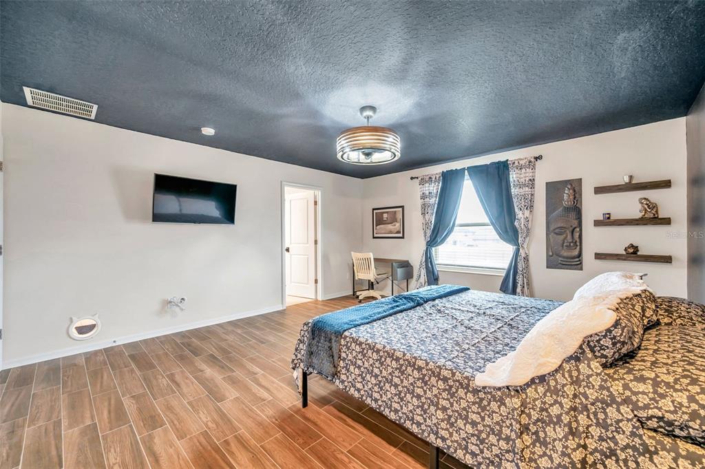 A bedroom features a dark ceiling, wood-look tile floors, a bed, and a wall-mounted television — 3737 COPPERSPRING BOULEVARD, NEW PORT RICHEY, FL