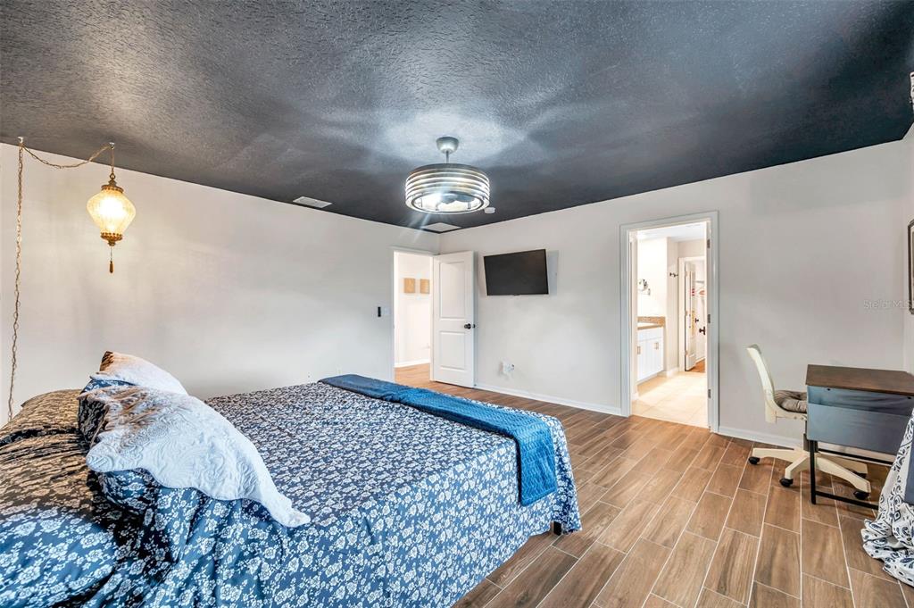 A bedroom features a dark ceiling, wood-look tile flooring, a bed with blue bedding, and two doorways — 3737 COPPERSPRING BOULEVARD, NEW PORT RICHEY, FL
