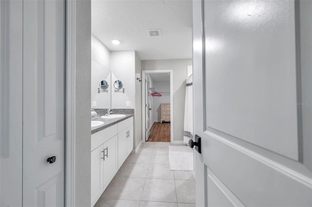 A bathroom with a double vanity, tiled floor, and an adjacent walk-in closet — 3737 COPPERSPRING BOULEVARD, NEW PORT RICHEY, FL