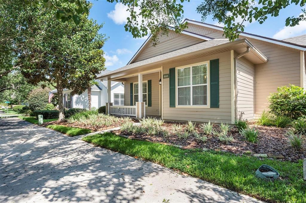 A tan house with green shutters and a front porch sits along a concrete sidewalk — 8668 SW 77TH AVENUE, GAINESVILLE, FL