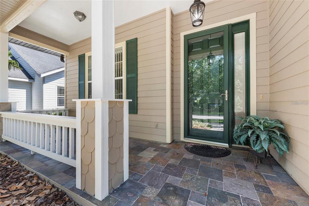 A covered front porch features slate-style tile flooring, a green front door, and beige siding — 8668 SW 77TH AVENUE, GAINESVILLE, FL
