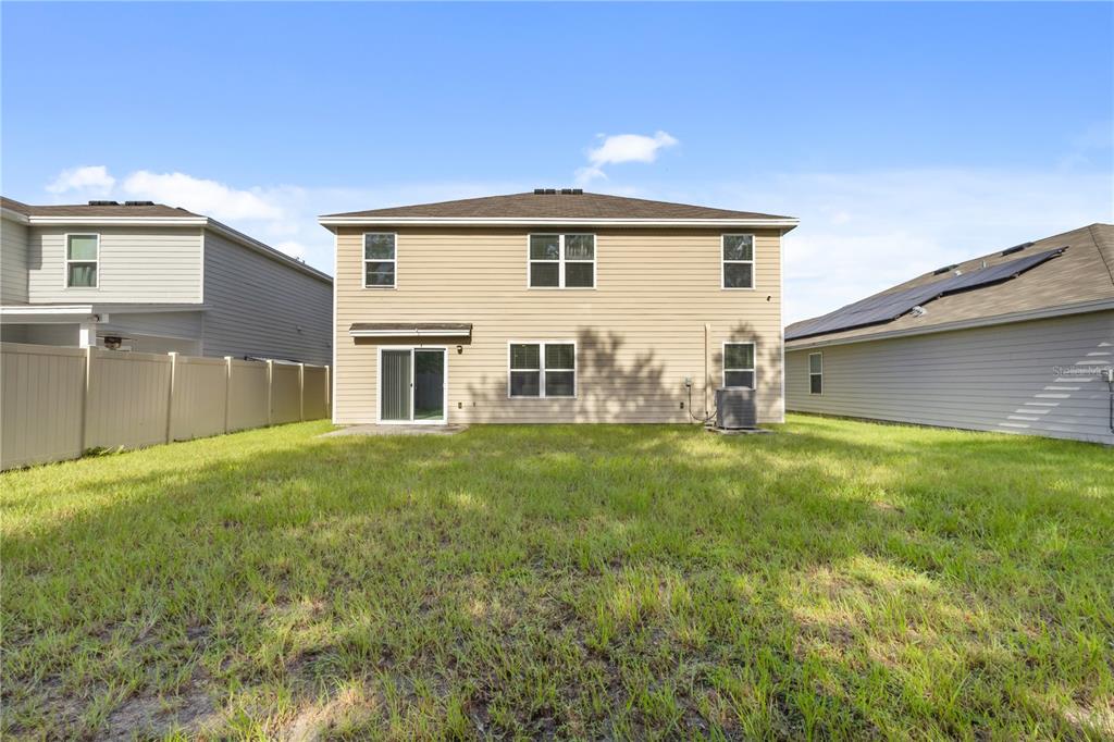 The rear exterior of a two-story tan house features a sliding glass door and lawn — 2143 NW 246TH TERRACE, NEWBERRY, FL