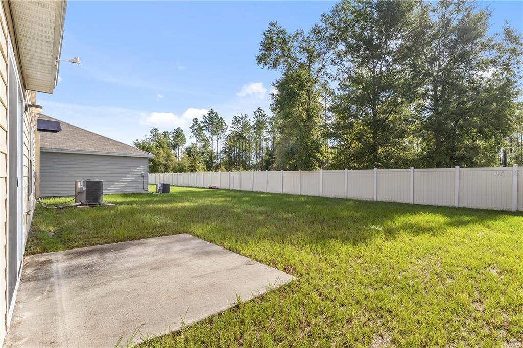 A concrete patio sits in a grassy backyard enclosed by a white vinyl fence — 2143 NW 246TH TERRACE, NEWBERRY, FL